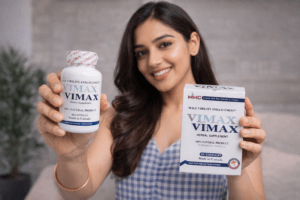 Confident young woman holding Vimax Capsule for Men bottle and box, smiling while promoting male virility herbal supplement for adultworldkart.com website.